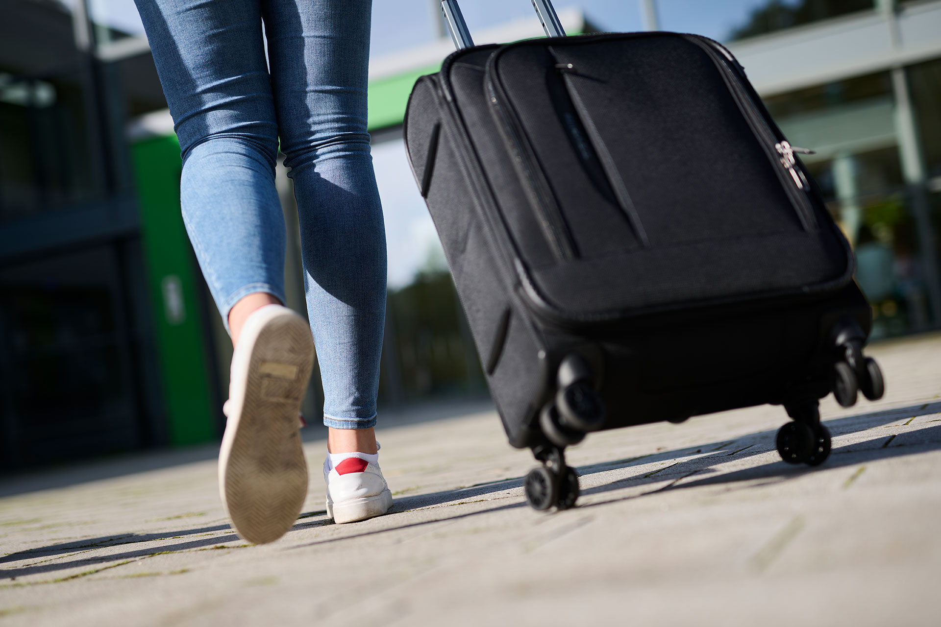 Ein Mädchen zieht einen schwarzen Koffer hinter sich her.