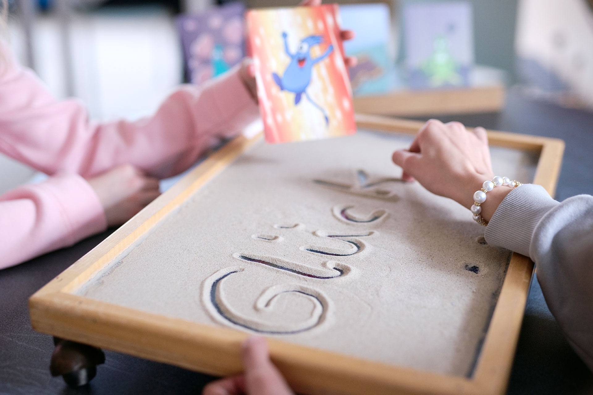 Zwei Kinder schreiben das Wort Glück in eine mit Sand gefüllte Kiste.