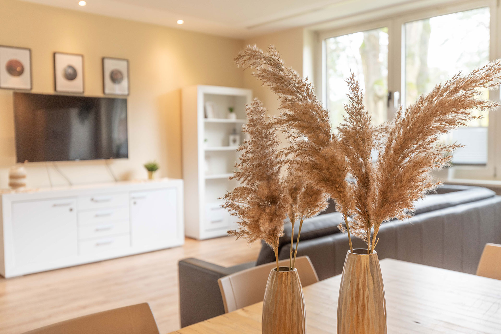 Wohnzimmer mit weißen Möbeln, im Vordergrund sind dekorative Trockenblumen zu sehen.