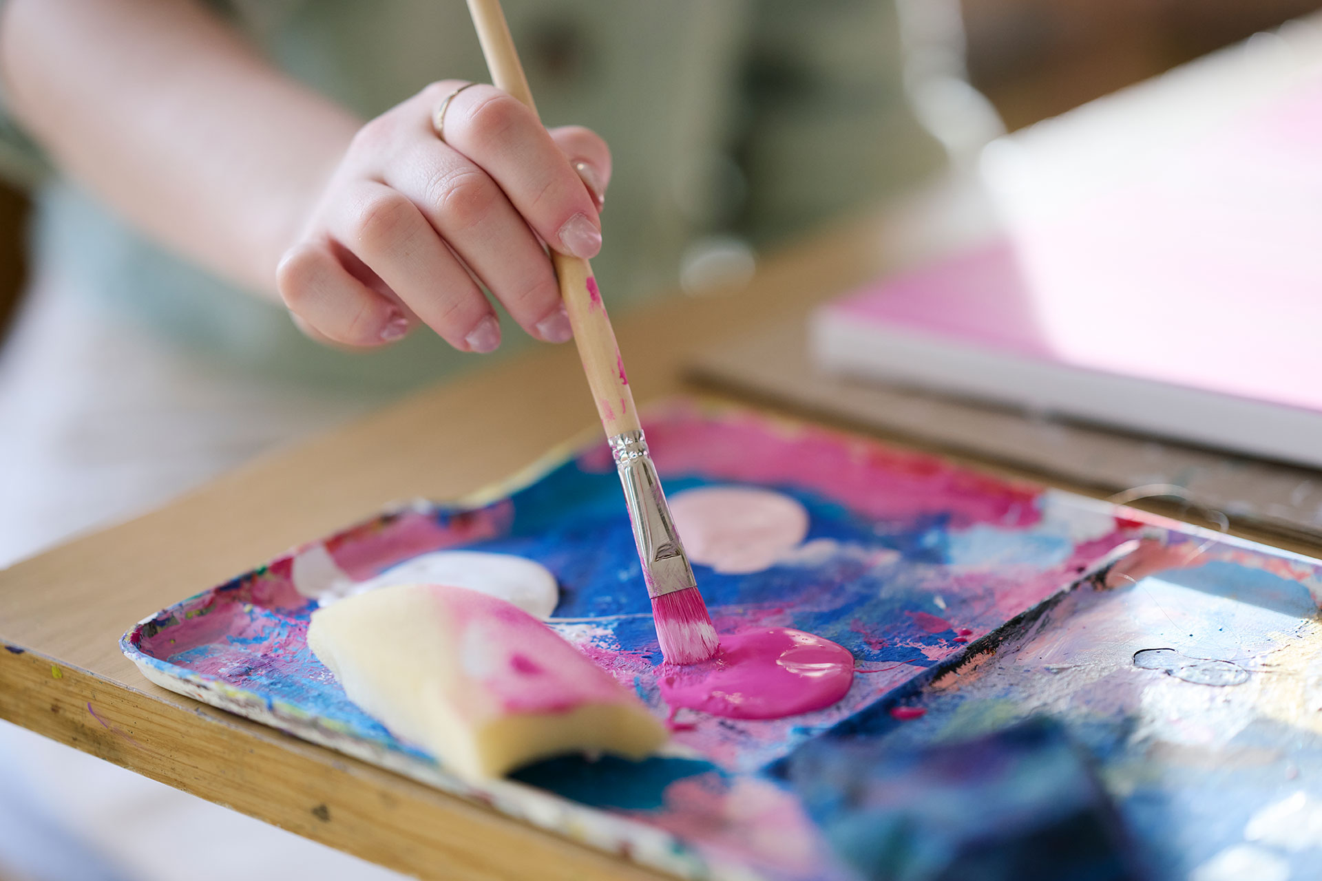 Ein Kind mal ein Bild, es tupft mit einem Pinsel in eine Farbe.