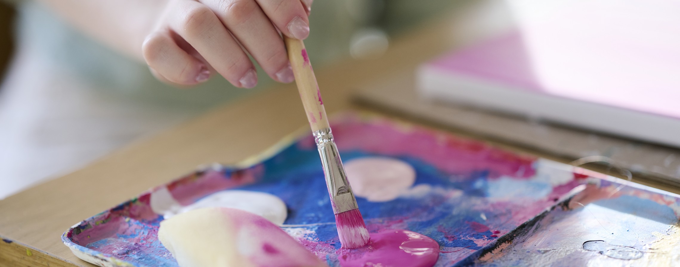 Ein Kind mal ein Bild, es tupft mit einem Pinsel in eine Farbe.