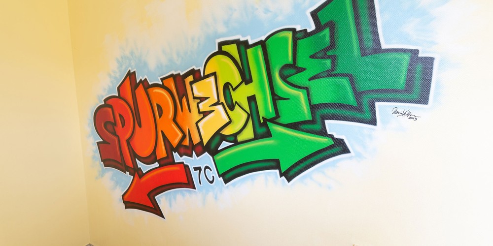 Das Bild zeigt ein Graffiti in einem Flur. In bunten Buchstaben steht das Wort "Spurwechsel" geschrieben.