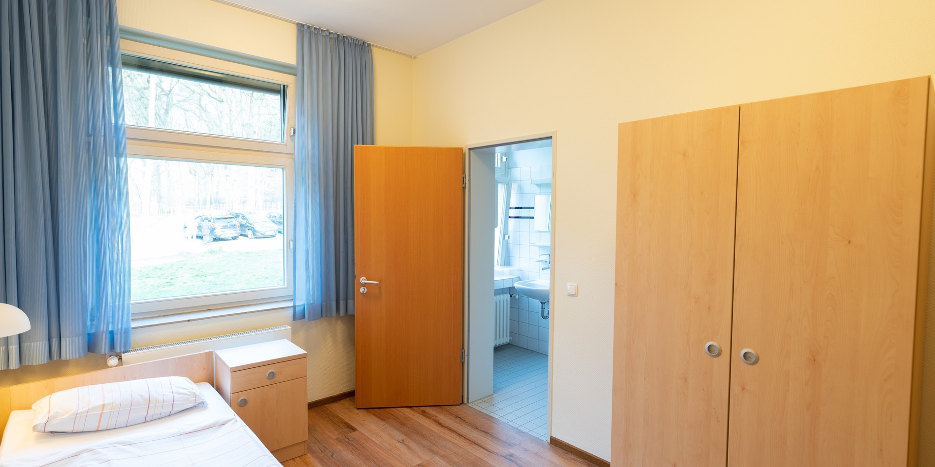 Das Bild zeigt ein Patientenzimmer mit einem Bett und einem Schrank.