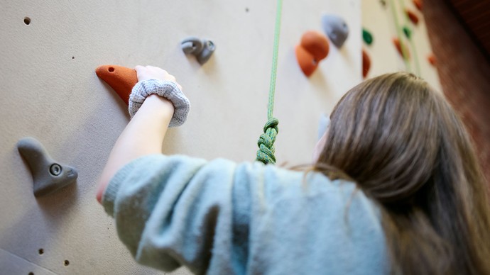 Ein Mädchen klettert an einer Kletterwand.