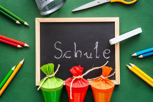 Das Bild zeigt drei Schultüten und eine Tafel, auf der das Wort "Schule" mit Kreide geschrieben steht.