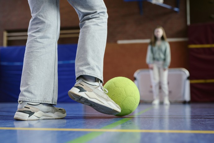 Zwei Personen spielen in einer Turnhalle Fußball.